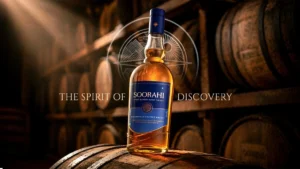 Premium Soorahi whisky bottle standing on a barrel with warm light highlighting its rich amber color in a whisky warehouse